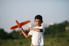 Little kid playing with airplane toy in green park